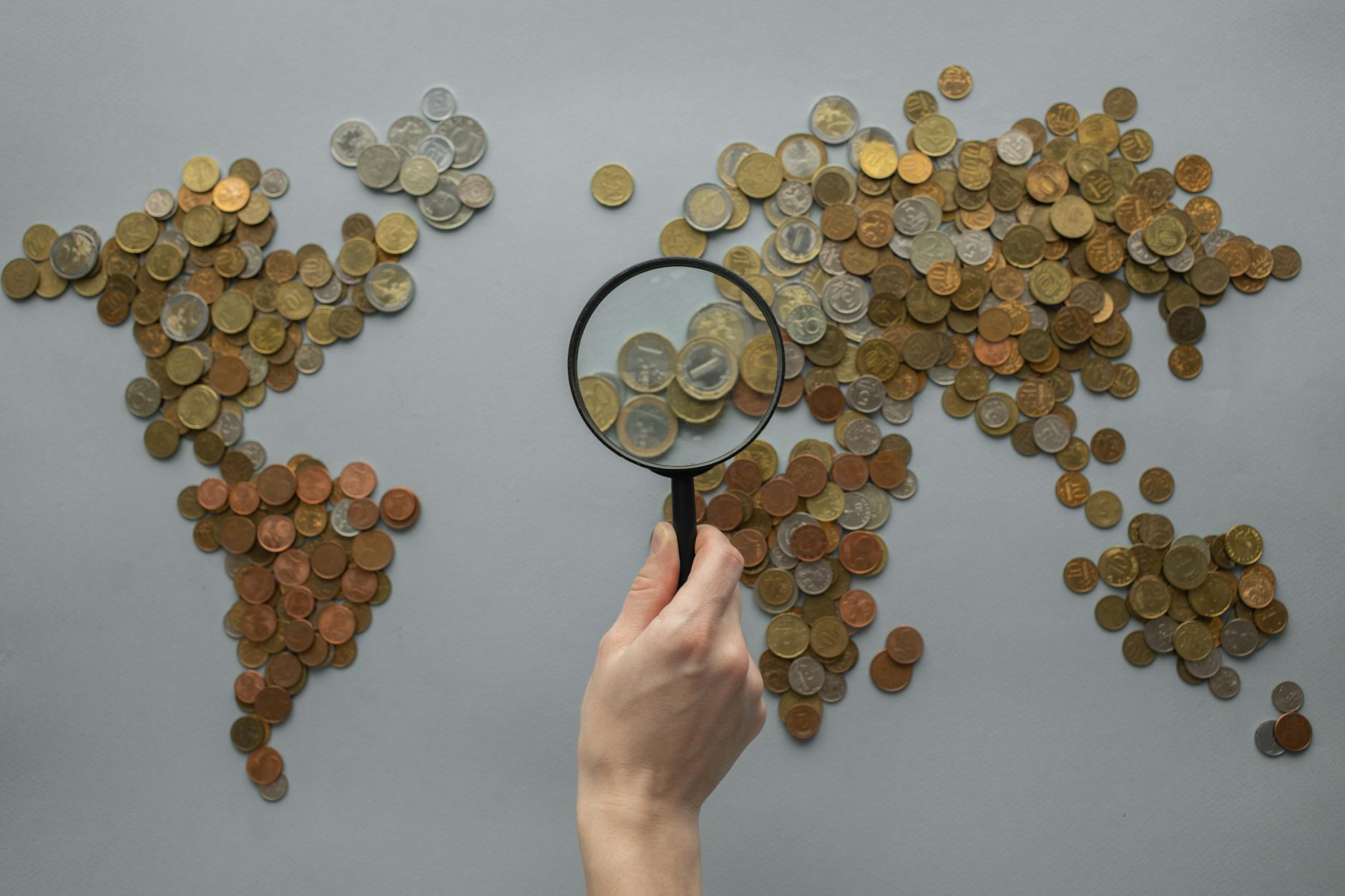 https://www.pexels.com/photo/anonymous-person-with-magnifying-glass-over-world-map-of-coins-7412089/