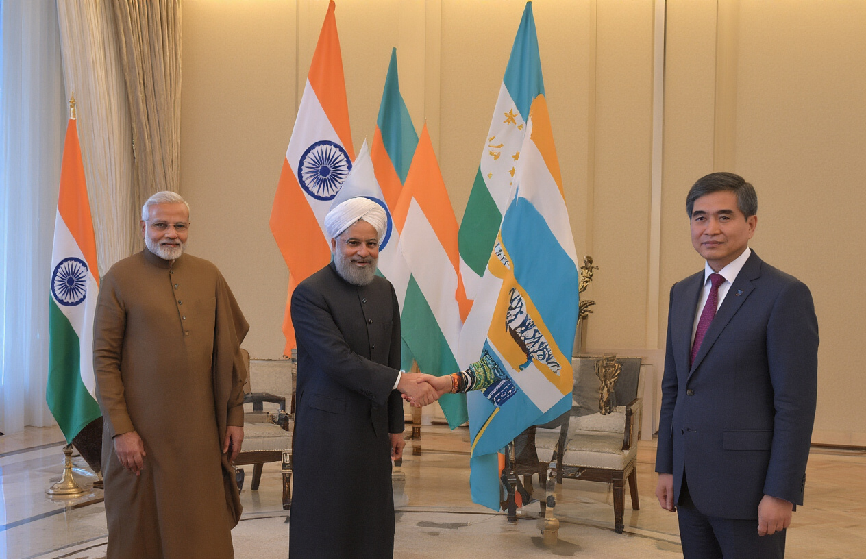 realistic image of two diplomatic figures, one South Asian male and one Central Asian male, shaking hands in a formal setting with the flags of India and Uzbekistan displayed prominently in the background, symbolizing a strong bilateral partnership, the scene is well-lit with warm, professional lighting conveying a sense of mutual respect and cooperation, with a polished conference room or government building interior as the backdrop. Absolutely NO text should be in the scene.