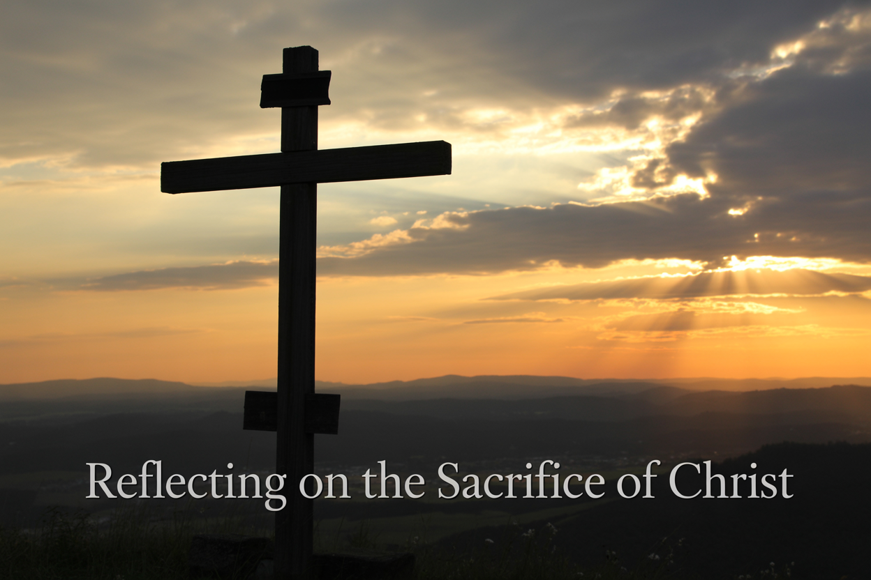 Create a realistic image of a wooden cross silhouetted against a dramatic sunset sky with golden and orange hues, positioned on a hill overlooking a peaceful landscape, with soft rays of light breaking through clouds and illuminating the cross, creating a serene and contemplative atmosphere that conveys hope and reverence, with the text "Reflecting on the Sacrifice of Christ" elegantly overlaid in white serif font at the bottom of the image.